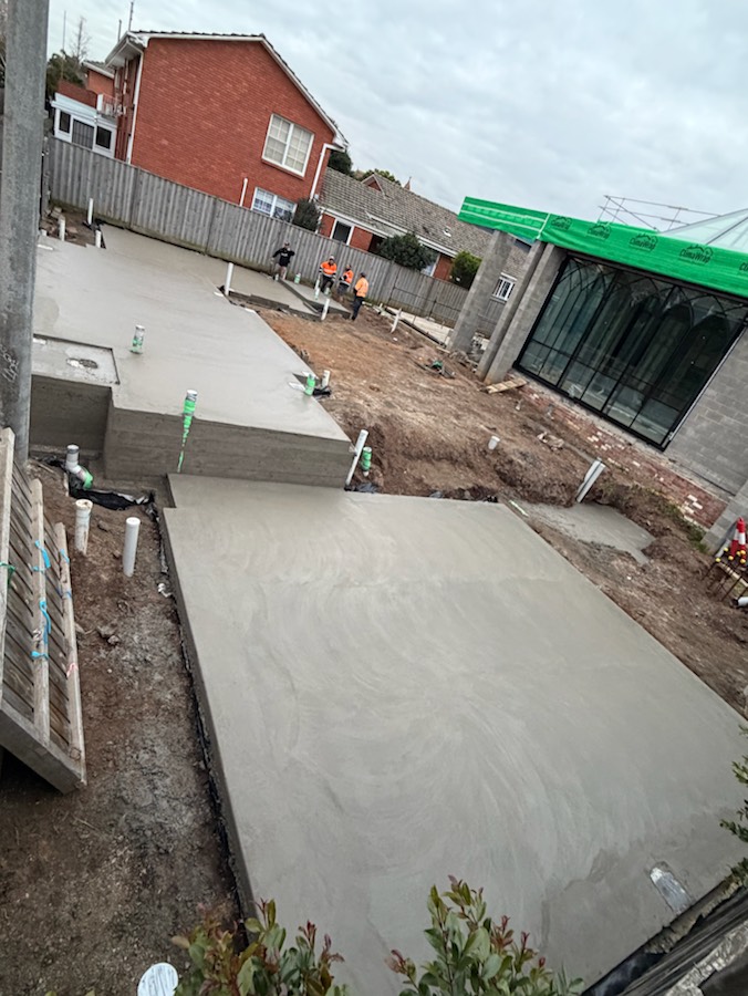 A split-level concrete slab beside a new build, with the crew working in the background